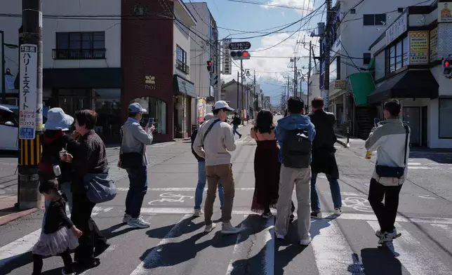 Foreign visitors stand to photograph Mount Fuji though Honcho Street on Wednesday, April 8, 2026, in Fujiyoshida, west of Tokyo. (AP Photo/Eugene Hoshiko)