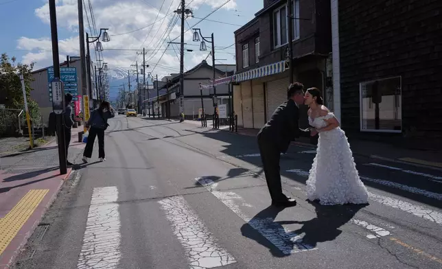 Foreign visitors pose for photos at Honcho Street with Mt. Fuji as background on Wednesday, April 8, 2026, in Fujiyoshida, west of Tokyo. (AP Photo/Eugene Hoshiko)