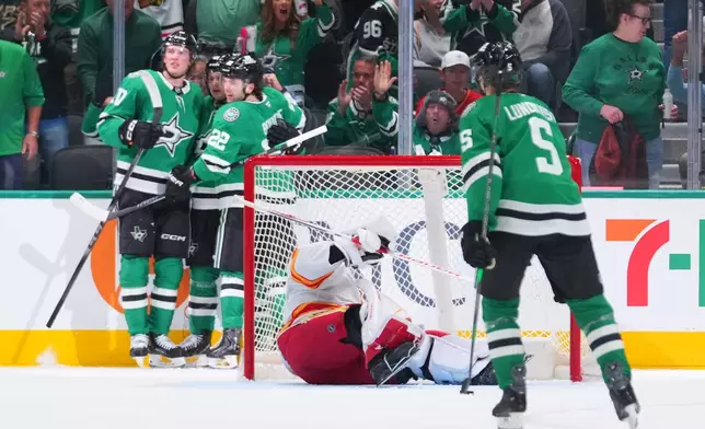 Calgary Flames goaltender Devin Cooley, center, is slow to get up as Dallas Stars players celebrate a second period goal by Justin Hryckowian during an NHL hockey game Tuesday, April 7, 2026, in Dallas. (AP Photo/Julio Cortez)