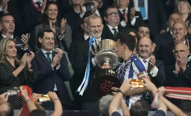 Spain's King Felipe VI, centre, looks as Real Sociedad's Mikel Oyarzabal kisses the trophy after the Copa del Rey final soccer match between Atletico Madrid and Real Sociedad in Seville, Spain, Saturday, April. 18, 2026. (AP Photo/Jose Breton)