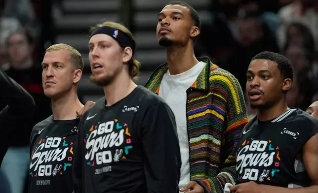 San Antonio Spurs forward Victor Wembanyama, center, wears street cloths on the bench as he sits out Game 3 of a first-round NBA playoffs basketball series against the Portland Trail Blazers in Portland, Ore, Friday, April 24, 2026. (AP Photo/Jenny Kane)