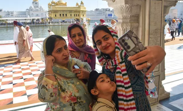 A family takes a selfie at the Golden Temple, Sikhism's holiest shrine, on Vaisakhi, a spring harvest festival for Sikhs and Hindus, in Amritsar, India, Tuesday, April 14, 2026. (AP Photo/Prabhjot Gill)