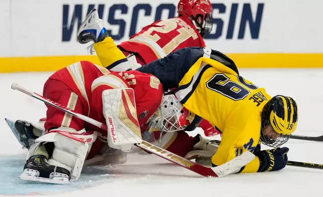 Michigan forward Michael Hage (19) falls on Denver goaltender Johnny Hicks (31) in the second period of a semifinal game of the NCAA Frozen Four men's college hockey tournament Thursday, April 9, 2026, in Las Vegas. (AP Photo/John Locher)