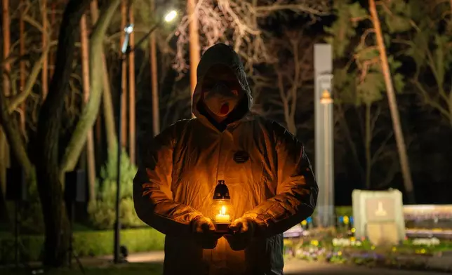 A man dressed in white protective suits holds a candle during a memorial service dedicated to firefighters and workers who died after the 1986 Chornobyl (Chernobyl) nuclear disaster, ahead of its 40th anniversary in Slavutych, Ukraine, Saturday, April 25, 2026.Chornobyl is the Ukrainian name for the city. (AP Photo/Dan Bashakov)