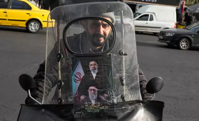 A man drives his motorbike with a poster on its windshield depicting Iran's Supreme Leader Ayatollah Mojtaba Khamenei, top, and his father, the slain Supreme Leader Ayatollah Ali Khamenei, who was killed in the U.S. and Israel strikes on Feb. 28, in downtown Tehran, Iran, Monday, April 13, 2026. (AP Photo/Vahid Salemi)