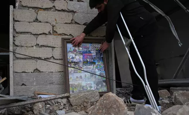 Ali Fahos, a member of Hezbollah's health unit, places portraits of colleagues killed during the previous war with Israel next to a building destroyed in an Israeli airstrike, in Jibchit, southern Lebanon, Friday, April 17, 2026, following a ceasefire between Israel and Hezbollah. (AP Photo/Hassan Ammar)