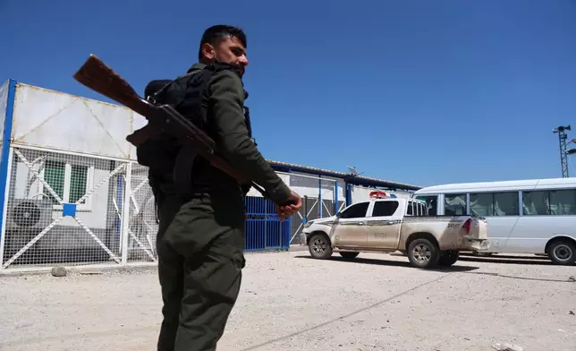 A soldier stands guard as vehicles arrive at Roj Camp in eastern Syria, housing people with alleged ties to Islamic State militants, to transport Australian families to Damascus as part of a second repatriation effort by Syrian authorities, Friday, April 24, 2026. (AP Photo/Baderkhan Ahmad)