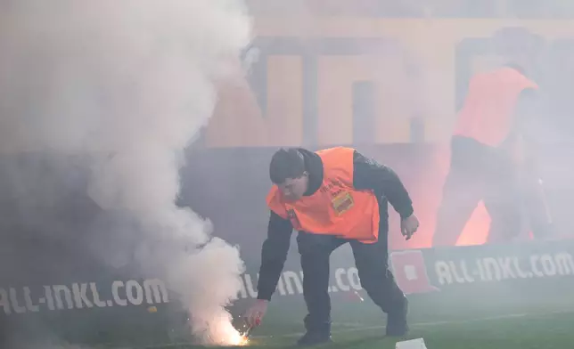 A steward removes burning pyrotechnics from the pitch during a stoppage in play in the Bundesliga 2 soccer match between Dynamo Dresden and Hertha BSC, Saturday, April 4, 2026, in Dresden, Germany. (Sebastian Kahnert/dpa via AP)