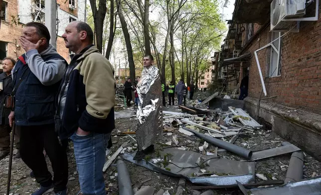 A man covered in thermal blanket stands in a yard of a residential building damaged by a Russian strike on Dnipro, Ukraine, Saturday, April 25, 2026. (AP Photo/Mykola Synelnykov)