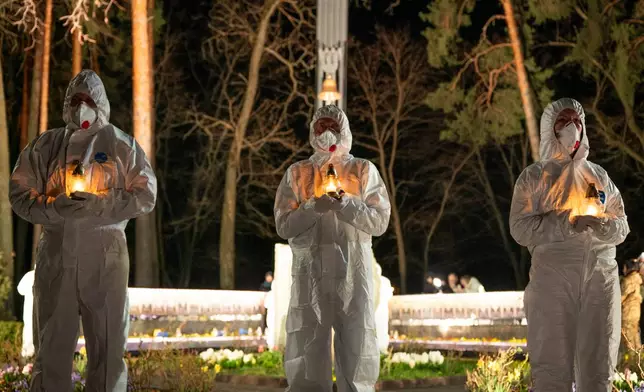People dressed in white protective suits hold candles during a memorial service dedicated to firefighters and workers who died after the 1986 Chornobyl (Chernobyl) nuclear disaster, ahead of its 40th anniversary in Slavutych, Ukraine, Saturday, April 25, 2026. Chornobyl is the Ukrainian name for the city. (AP Photo/Dan Bashakov)