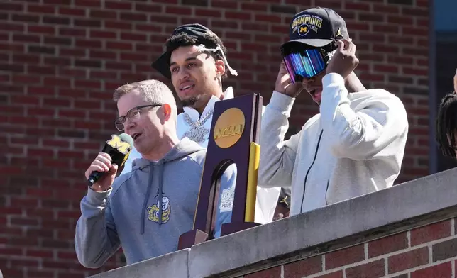 Michigan head coach Dusty May, left, talks to fans as Yaxel Lendeborg, center, and L.J. Cason, right, listen as the team returns to campus Tuesday, April 7, 2026, in Ann Arbor, Mich., the day after defeating UConn at the Final Four of the NCAA college basketball tournament. (AP Photo/Paul Sancya)