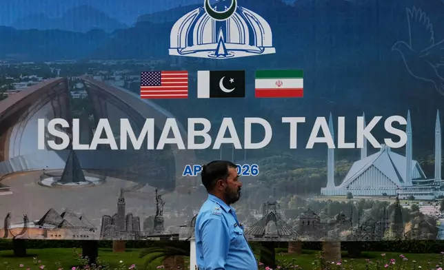 A police officer walks past a billboard regarding the United States and Iran negotiations, outside a media facilitation center in Islamabad, Pakistan, Saturday, April 11, 2026. (AP Photo/Anjum Naveed)