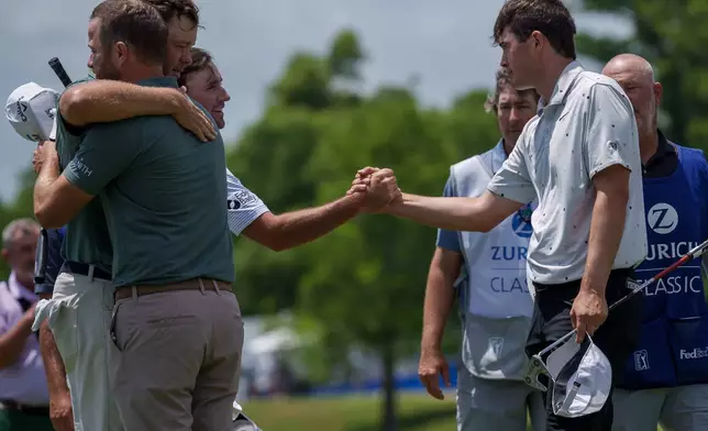 Austin Eckroat, background left, shakes hands with Davis Thompson reacts after missing a putt while Chris Kirk, first left, and Patton Kizzire embrace on the 18th hole during the first round of the PGA Zurich Classic golf tournament, Thursday, April 23, 2026, in Avondale, La. (AP Photo/Matthew Hinton)