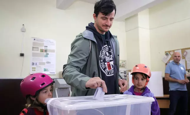 A father casts his ballot, accompanied by his daughters at a polling station in Sofia on Sunday, April 19, 2026, during early parliamentary elections. (AP Photo/Valentina Petrova)