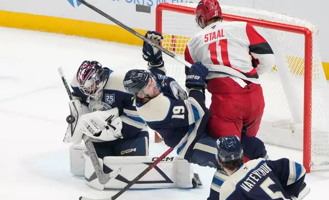 Columbus Blue Jackets goaltender Jet Greaves, left, blocks a shot as Carolina Hurricanes center Jordan Staal (11) checks center Adam Fantilli (19) in the second period of an NHL game in Columbus, Tuesday, March 31, 2026. (AP Photo/Sue Ogrocki)