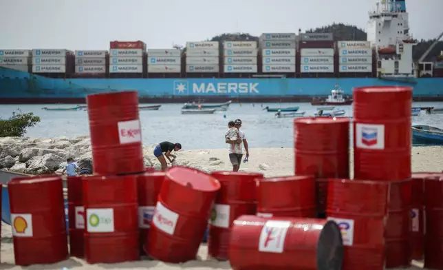 A family walks near a Make Polluters Pay demonstration along the Caribbean Sea demanding oil companies pay for the energy transition during a nearby conference aimed at transitioning away from fossil fuels Monday, April 27, 2026, in Santa Marta, Colombia. (AP Photo/Ivan Valencia)