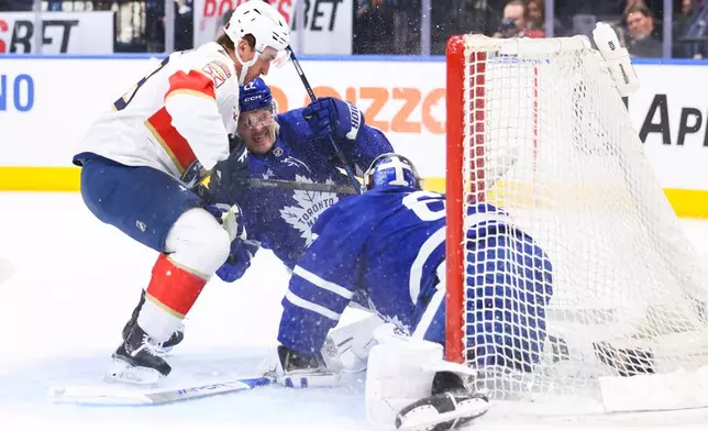 Florida Panthers' Cole Reinhardt, left, collides with Toronto Maple Leafs' Jake McCabe (22) in front of Maple Leafs goaltender Joseph Woll, right, during first-period NHL hockey game action in Toronto, Saturday, April 11, 2026. (Cole Burston/The Canadian Press via AP)