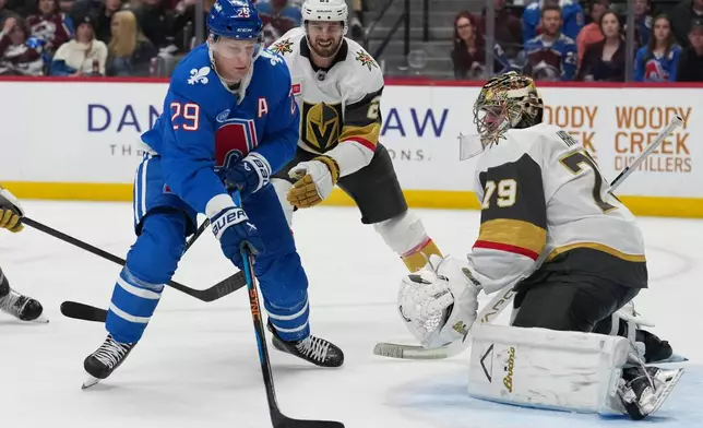 Colorado Avalanche center Nathan MacKinnon, left, puts a shot on Vegas Golden Knights goaltender Carter Hart, right, after driving past defenseman Shea Theodore in the third period of an NHL hockey game Saturday, April 11, 2026, in Denver. (AP Photo/David Zalubowski)