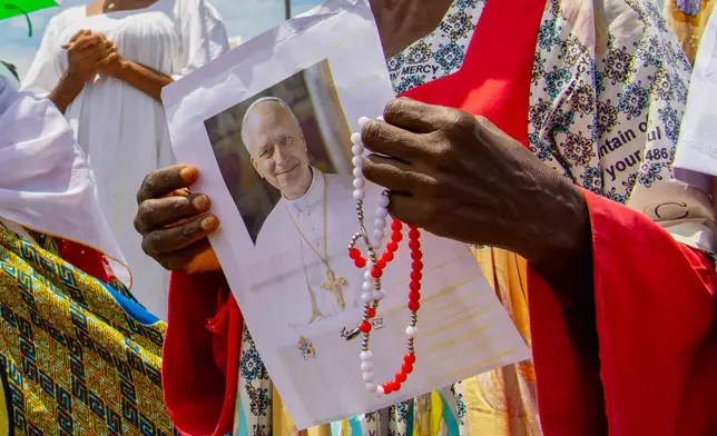 A Catholic faithful holds an image of Pope Leo XIV as she waits for his arrival at Yaounde Nsimalen International Airport in Yaounde, Cameroon, Wednesday, April 15, 2026. (AP Photo/Welba Yamo Pascal)