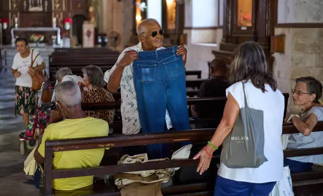 Carlos Lugo, 82, shows off a pair of jeans he received from charity before entering the dining hall adjacent to the Church of the Holy Spirit, where a church-run program offers free meals to seniors three times a week, in Old Havana, Wednesday, April 15, 2026. (AP Photo/Ramon Espinosa)