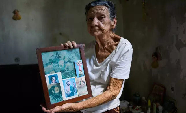 Mercedes Lopez Rey holds a framed cyanotype with an image of the late Cuban President Fidel Castro and prayer cards tucked into the edges of the frame, in her home in Old Havana, Cuba, Friday, April 10, 2026. (AP Photo/Ramon Espinosa)