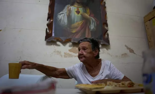 Mercedes Lopez Rey, 83, holds out her cup to be filled with water in a dining hall adjacent to the Church of the Holy Spirit, where a church-run program provides free meals to seniors three times a week, in Old Havana, Cuba, Friday, April 10, 2026. (AP Photo/Ramon Espinosa)