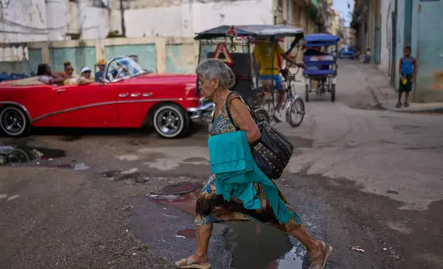 A woman steps over a puddle while walking through Old Havana, Cuba, Saturday, Feb. 15, 2025. (AP Photo/Ramon Espinosa)