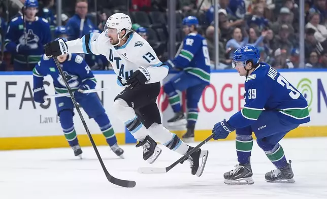 Utah Mammoth's Brandon Tanev (13) leaps past Vancouver Canucks' Ty Mueller (39) as he chases down the loose puck during the second period of an NHL hockey game, in Vancouver, on Saturday, April 4, 2026. (Darryl Dyck/The Canadian Press via AP)