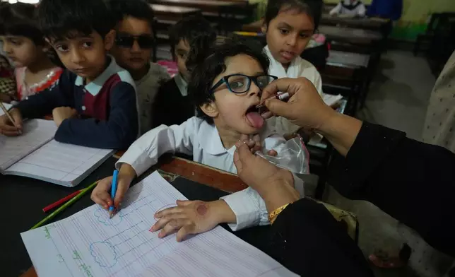 A health worker administers a polio vaccine to a child at a school in Lahore, Pakistan, Monday, April 13, 2026. (AP Photo/K.M. Chaudary)