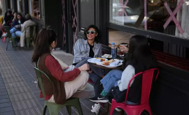 Three young girls sit together over soft drinks and sandwiches at a café terrace in Tehran, Iran, Wednesday, April 8, 2026. (AP Photo/Francisco Seco)