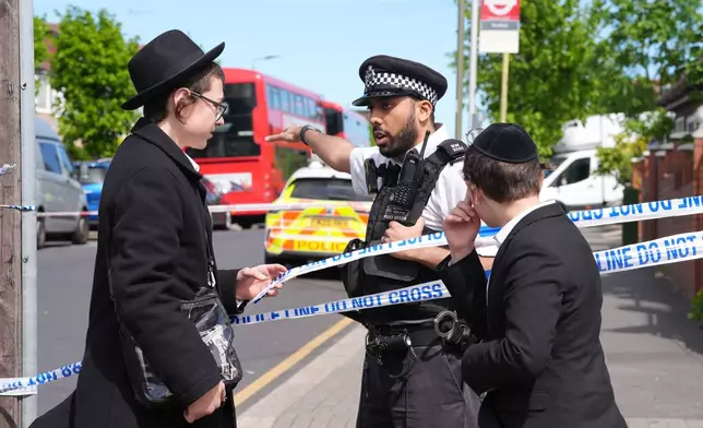 A Police officer talks with two boys at the scene where two people were stabbed Wednesday April 29, 2026 in a London neighborhood with a large Jewish community and a 45-year-old man was arrested on suspicion of attempted murder over what authorities called an antisemitic attack. (Lucy North/PA via AP)