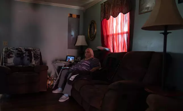 Rebecca Michalski, who recently took out a loan to pay her electric bills, sits with her Chihuahua named Enos in the dark in her home in Rainelle, W.Va., Saturday, March 21, 2026. (AP Photo/Carolyn Kaster)