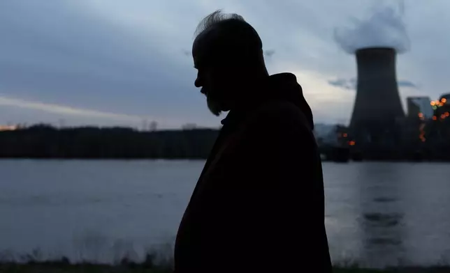 Eric Pinson, manager and resident of the Lock 24 RV Park and Campground, one of two such locations he manages in the area, is silhouetted at dusk as the coal-fired Mountaineer Power Plant, near New Haven, W.Va., stands across the Ohio River from the campground, Friday, March 13, 2026, in Racine, Ohio. (AP Photo/Carolyn Kaster)