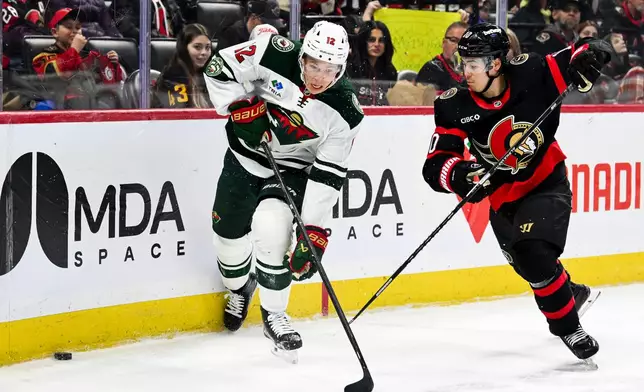 Minnesota Wild's Matt Boldy (12) and Ottawa Senators' Jordan Spence (10) fight for control of the puck along the boards during the first period of an NHL hockey game, Saturday, April 4, 2026, in Ottawa, Ontario. (Spencer Colby/The Canadian Press via AP)