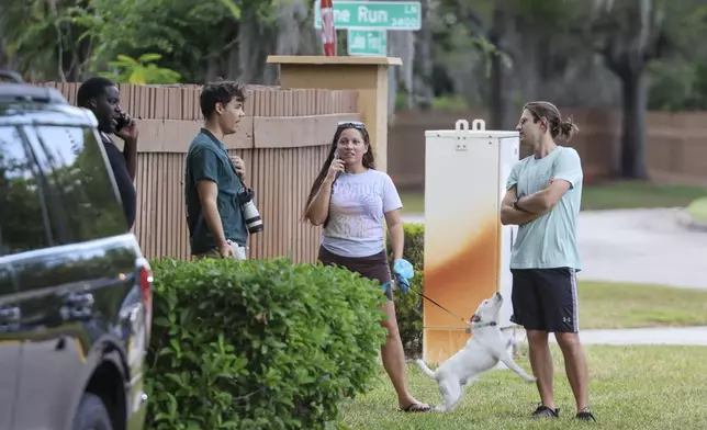 People gather near the entrance of the Lake Forest subdivision of Tampa, Fla., on Friday, April 24, 2026, where authorities said a man was taken into custody after barricading himself inside a home, in connection to the search for two missing University of South Florida graduate students. (Douglas R. Clifford/Tampa Bay Times via AP)