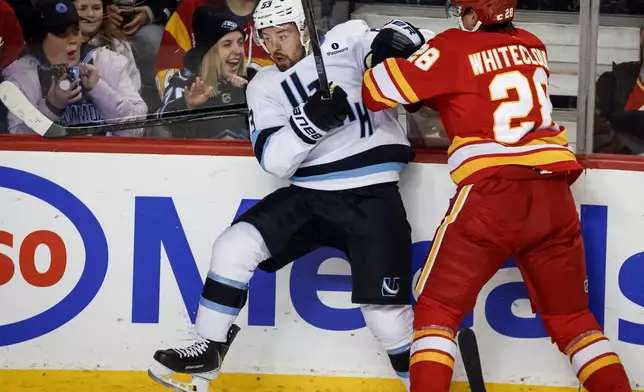 Utah Mammoth's Michael Carcone, left, is checked by Calgary Flames' Zach Whitecloud during first period NHL hockey action in Calgary, Alberta, Sunday, April 12, 2026. (Jeff McIntosh/The Canadian Press via AP)