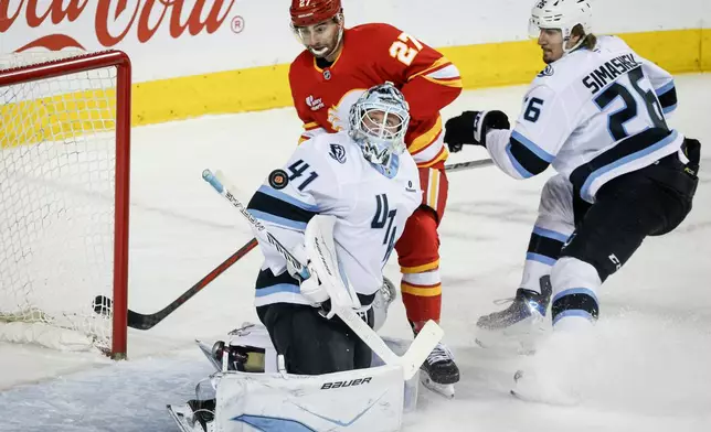 Utah Mammoth goalie Vitek Vanecek, centre, follows the puck as Calgary Flames' Matt Coronato, left, and Dmitri Simashev look on during first period NHL hockey action in Calgary, Alberta, Sunday, April 12, 2026. (Jeff McIntosh/The Canadian Press via AP)
