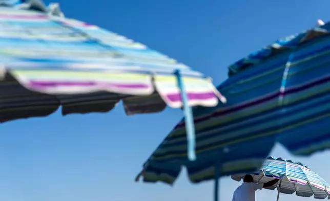 FILE - A resort worker folds up beach umbrellas Aug. 16, 2025, in South Yarmouth, Mass. (AP Photo/David Goldman, File)