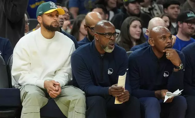 Injured Golden State Warriors guard Stephen Curry, left, watches from the bench with assistant coaches Kris Weems, middle, and Jerry Stackhouse during the first half of an NBA basketball game against the Cleveland Cavaliers in San Francisco, Thursday, April 2, 2026. (AP Photo/Jeff Chiu)