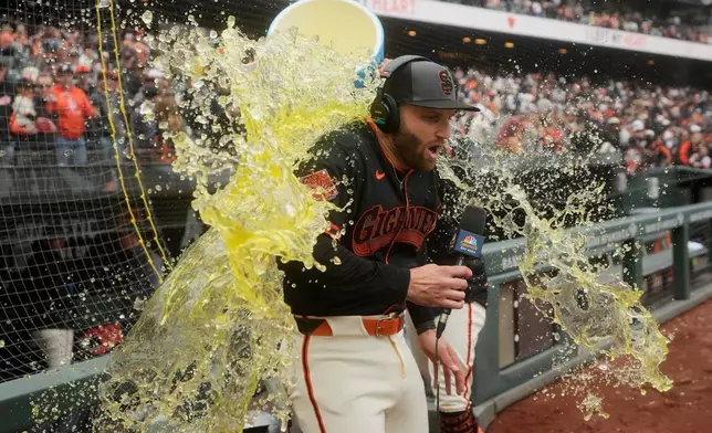 San Francisco Giants' Casey Schmitt is doused by Willy Adames while being interviewed after a baseball game against the Miami Marlins Saturday, April 25, 2026, in San Francisco. (AP Photo/Jeff Chiu)