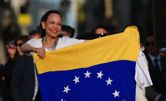 Venezuela's opposition leader Maria Corina Machado holds a Venezuelan flag on stage in front of supporters at Madrid's Puerta del Sol, in Madrid, Spain, Saturday, April 18, 2026. (AP Photo/Manu Fernandez)