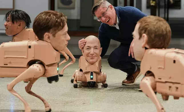 Artist Beeple, Mike Winkelmann, poses inside his installation titled Regular Animals, with robots in the likeness of Kim Jong Un, left, Elon Musk, second left, Kim Jong Un, Jeff Bezos, center, and Mark Zuckerberg, right, at the Neue Nationalgalerie museum in Berlin, Germany, Tuesday, April 28, 2026. (AP Photo/Markus Schreiber)