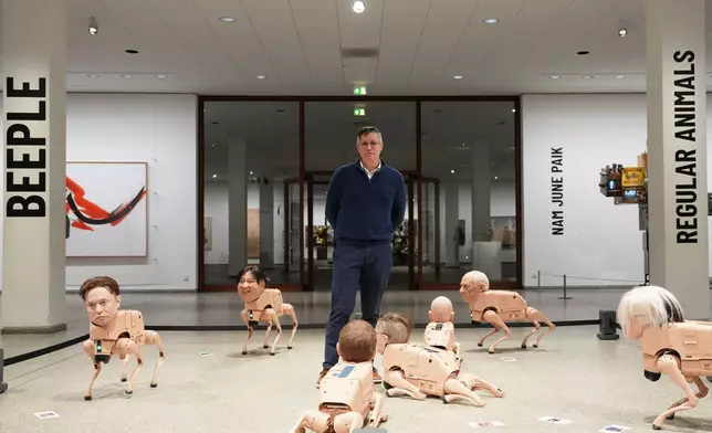 Artist Beeple, Mike Winkelmann, poses inside his installation titled Regular Animals, with robots in the likeness of Elon Musk, left, Kim Jong Un, second left, Pablo Picasso, second right, and Andy Warhol, right, at the Neue Nationalgalerie museum in Berlin, Germany, Tuesday, April 28, 2026. (AP Photo/Markus Schreiber)