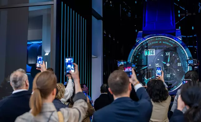 Visitors take photos with their smartphones of a watch at the German watch manufacturer A. Lange &amp; Shone stand, during the opening day of the "Watches and Wonders Geneva" luxury watch fair, in Geneva, Switzerland, Tuesday, April 14, 2026. (Salvatore Di Nolfi/Keystone via AP)