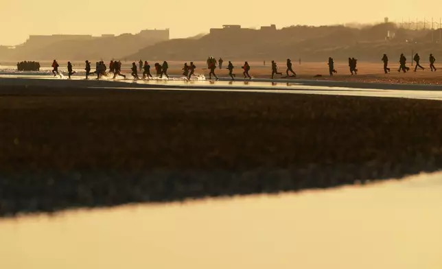 Migrants run to board a small boat in an attempt to reach Britain, Wednesday, April 8, 2026 in Malo-les-Bains, northern France. (AP Photo/Jean-Francois Badias)