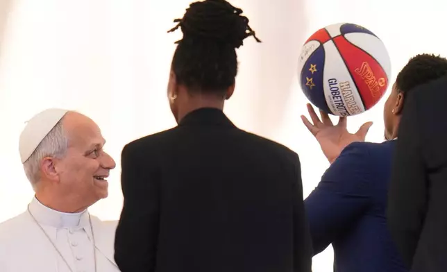 Pope Leo XIV looks at a basketball as he meets athletes from the Harlem Globetrotters who attended his weekly general audience in St. Peter's Square, at the Vatican, Wednesday, April 8, 2026. (AP Photo/Gregorio Borgia)
