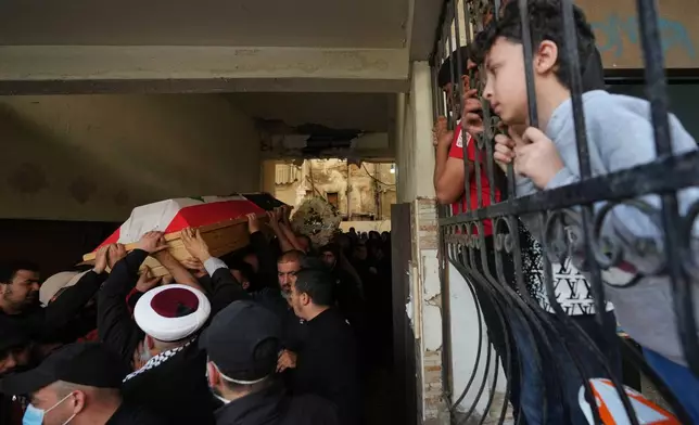 Mourners carry the coffin of Palestinian fighter Hozeifa Hamza Ghannamieh, who was killed alongside Ibrahim Anwar al-Khalayli while fighting alongside Hezbollah against Israel in southern Lebanon, during their funeral procession as children watch from behind a fence in Beirut, Lebanon, Tuesday, April 28, 2026. (AP Photo/Hassan Ammar)