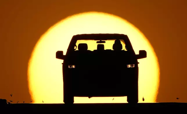A motorist is silhouetted by the setting sun as the region hit a high temperature to tie a record for the hottest day in March in the area, Thursday, March 26, 2026, in Lenexa, Kan. (AP Photo/Charlie Riedel)