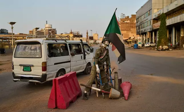 A minibus drives past an empty checkpoint where a mannequin dressed as a soldier stands in downtown Khartoum, Sudan, Sunday, April 19, 2026. (AP Photo/Bernat Armangue)
