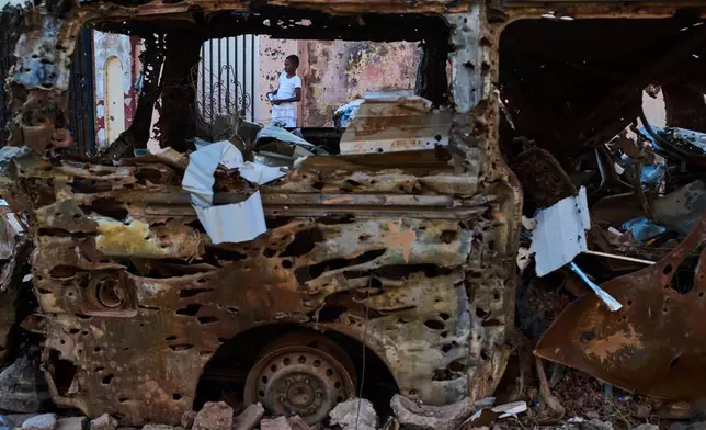 A boy is seen through the wreckage of a car in Omdurman, Sudan, on the outskirts of Khartoum, Friday, April 17, 2026. (AP Photo/Bernat Armangue)